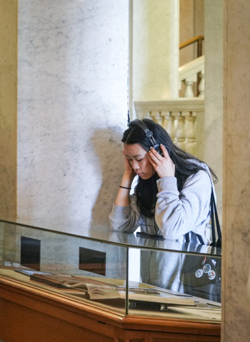 a student listens with headphones and watches to a video in an exhibit case