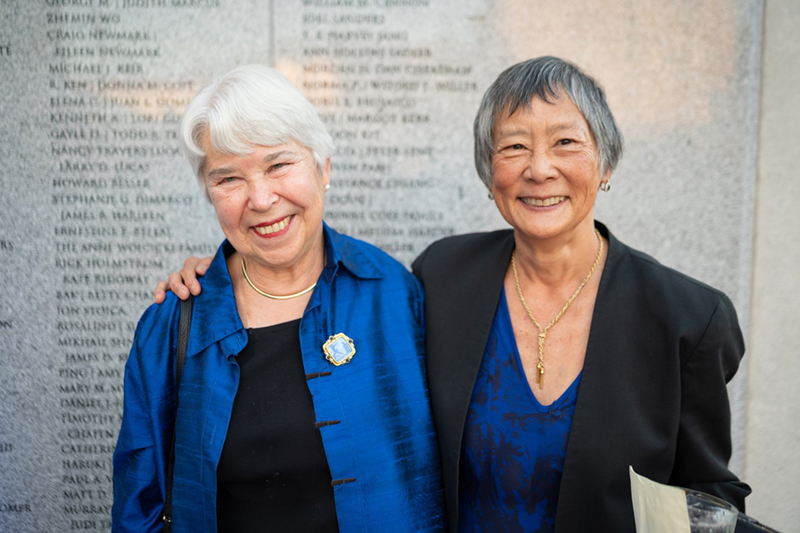 two women smile at the camera, one with her arm around the other