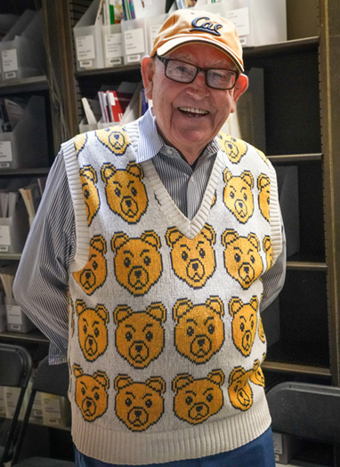 a man smiles at the camera while wearing a sweater covered in bears. 