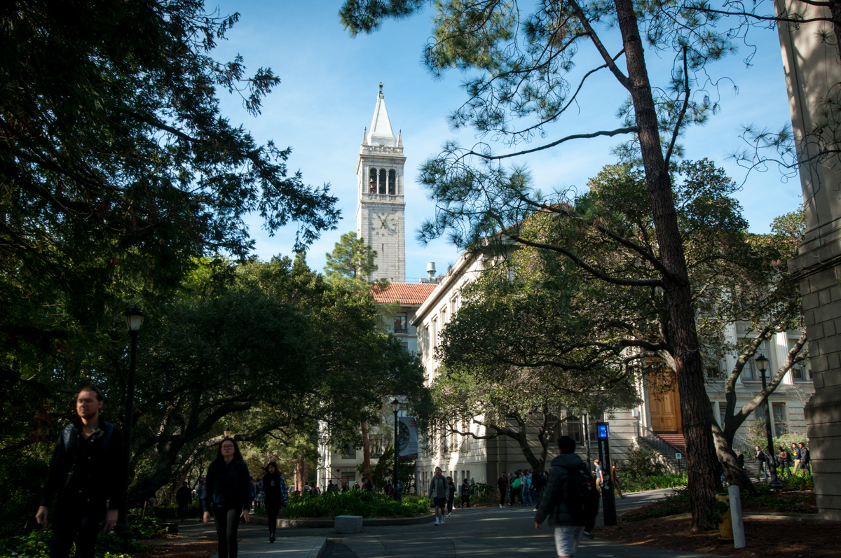 The campanile rises above campus and a line of people walking