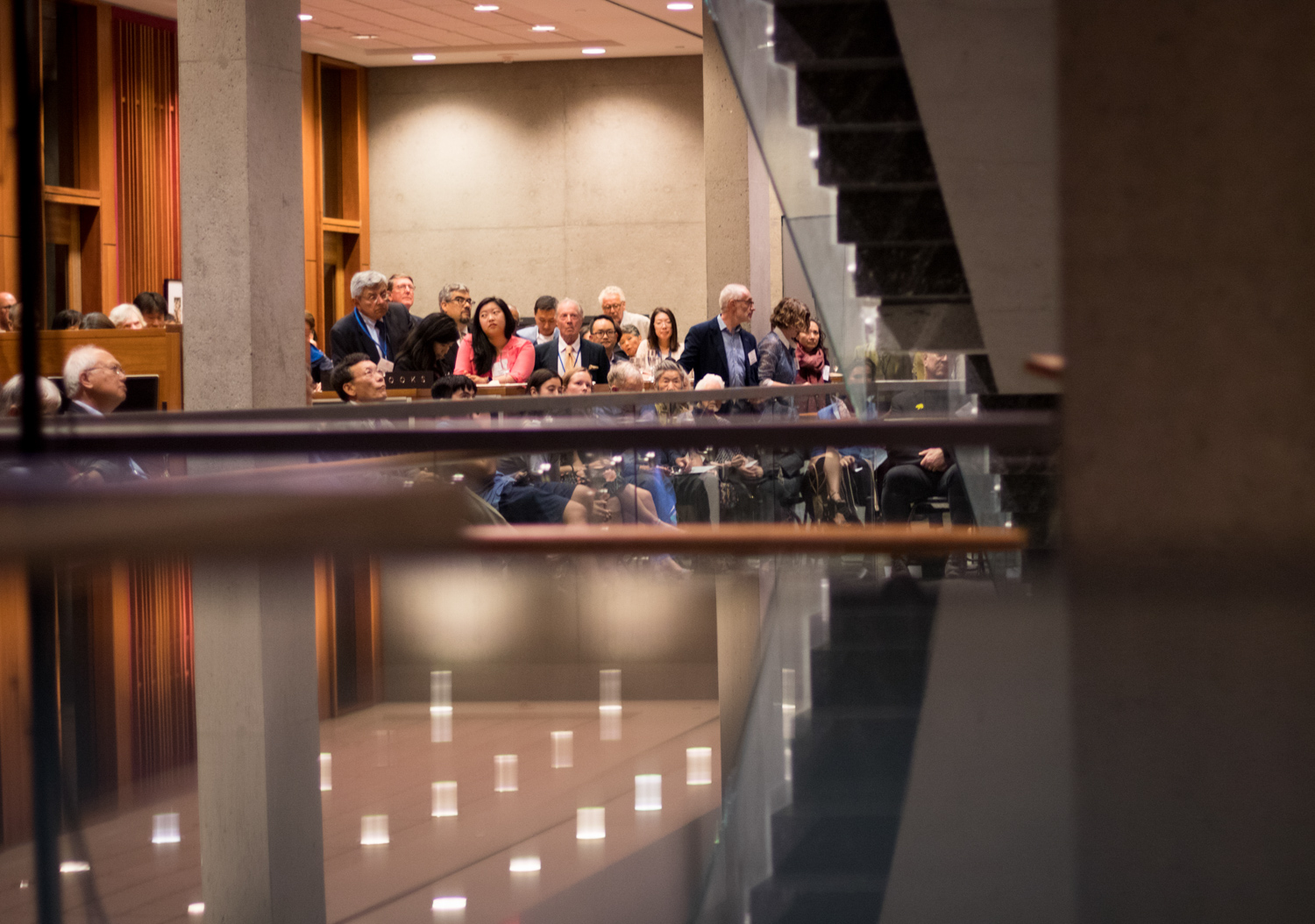 people listen to a speaker at an event, with lights reflected in glass