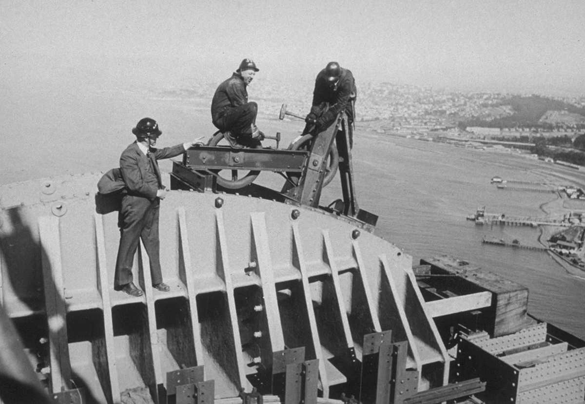 man in hard hats balance high on a part of the bridge, working