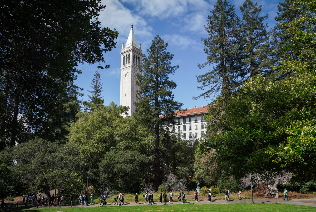 The campanile rises above campus and a line of people walking