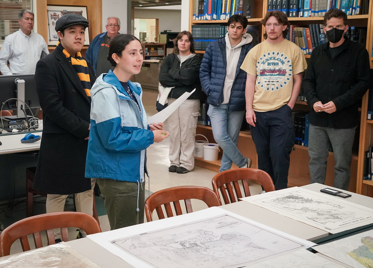 a student gives a presentation in front of a table of maps