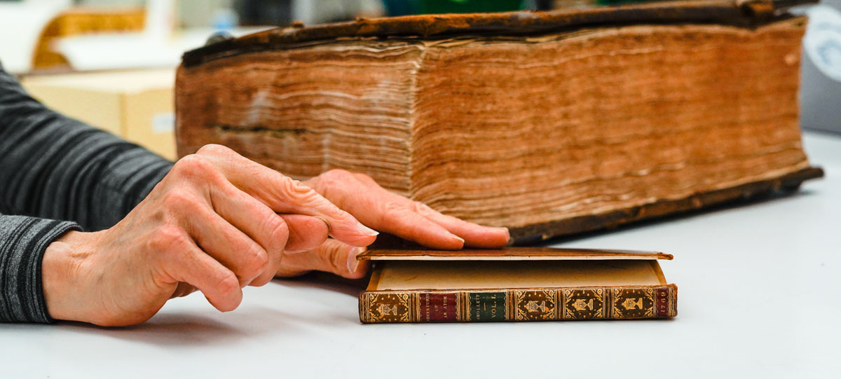 A hand points to a book cover that is falling off a book