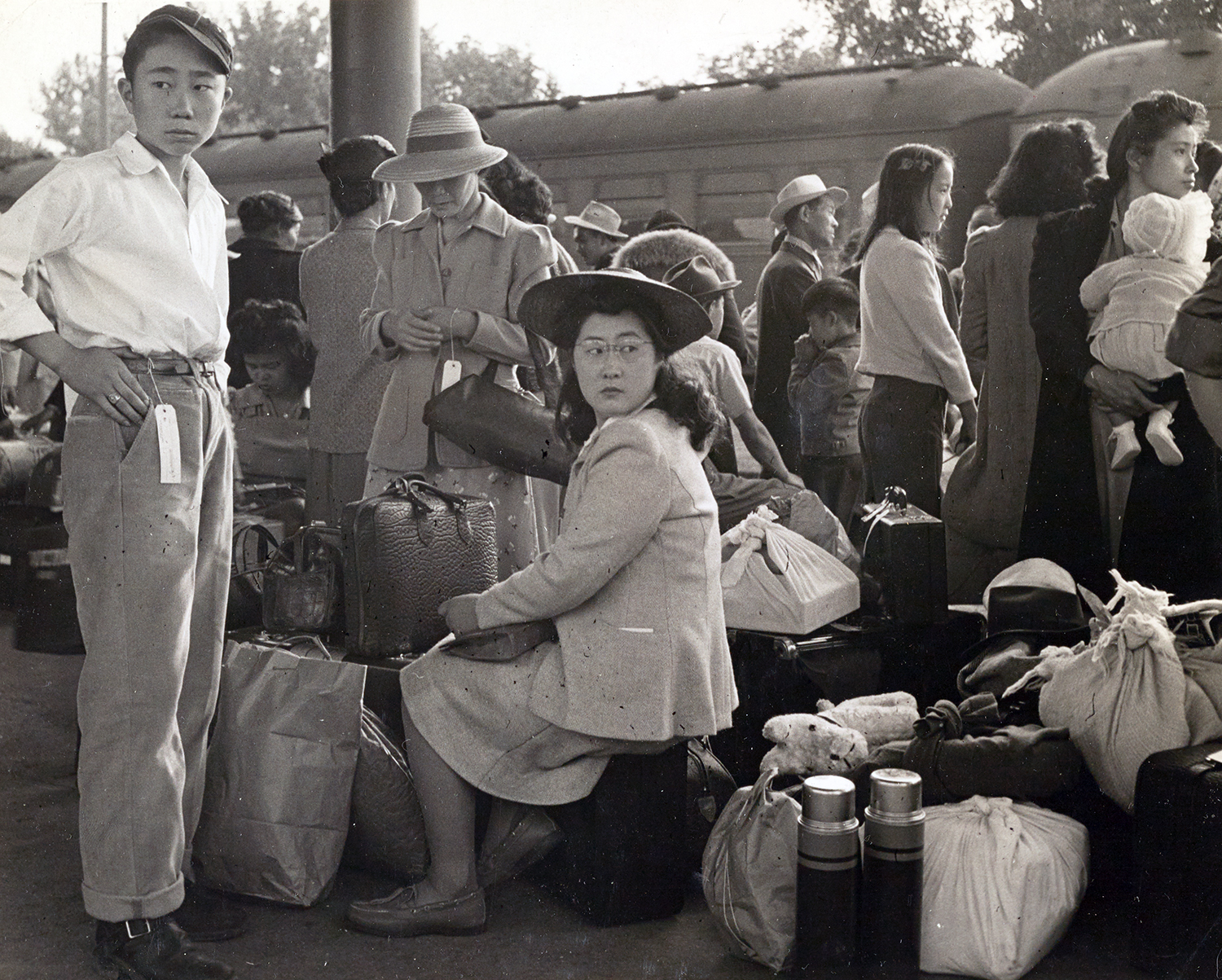 Japanese-Americans with luggage await transport. 