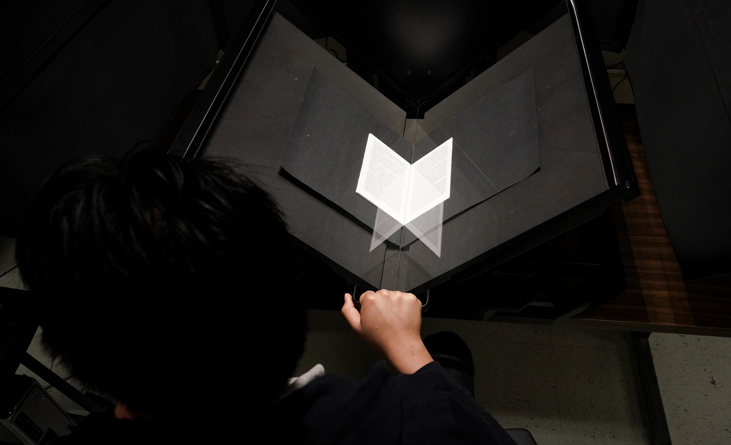 The Selfish Gene, the book being digitized, is reflected in glass as Perez works.