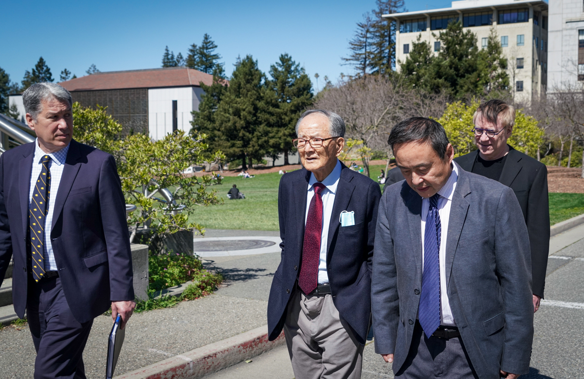 four men walk on campus with the East Asian Library in the background