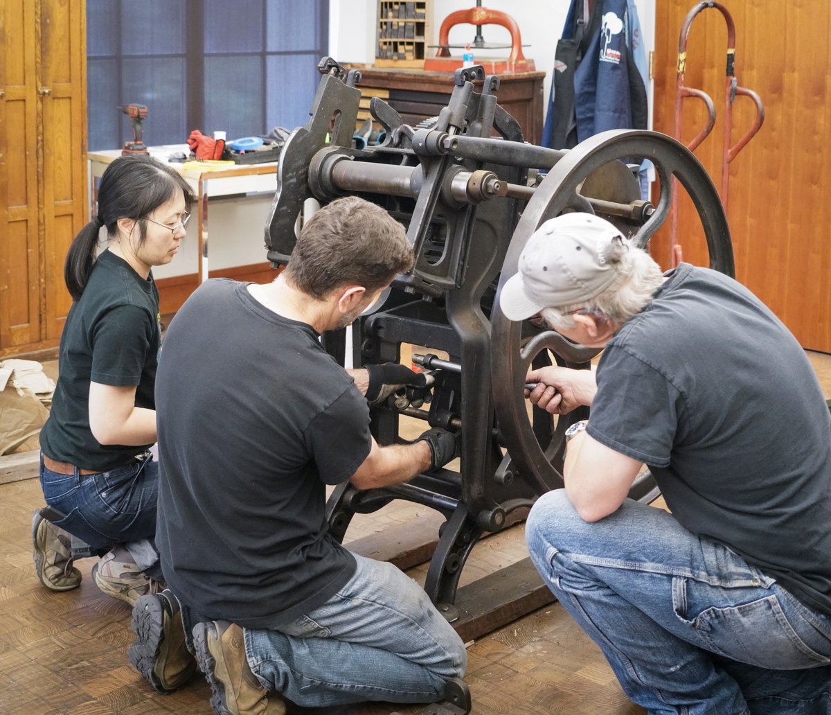 three people work on an old press together