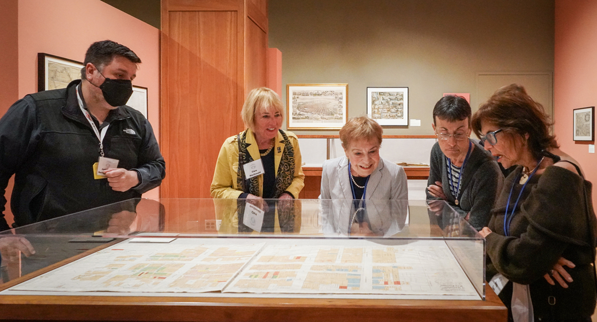 A group of people look at maps in a glass table 